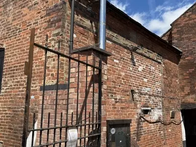 Nilfisk DTE static pressure washer fitted with a stainless steel flue extension at a brewery in Burton, installed to safely redirect boiler exhaust fumes away from a confined courtyard cleaning area.